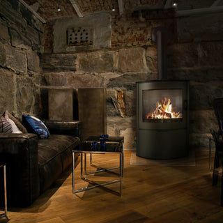 en svart  braskaminens från framsidan, i kammaren på braskaminen är det eld. på vänster sida är det en soffa och ett litet bord